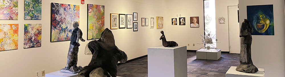 The installation of the artwork in the gallery. Art hangs on the walls and stands on pedestals.